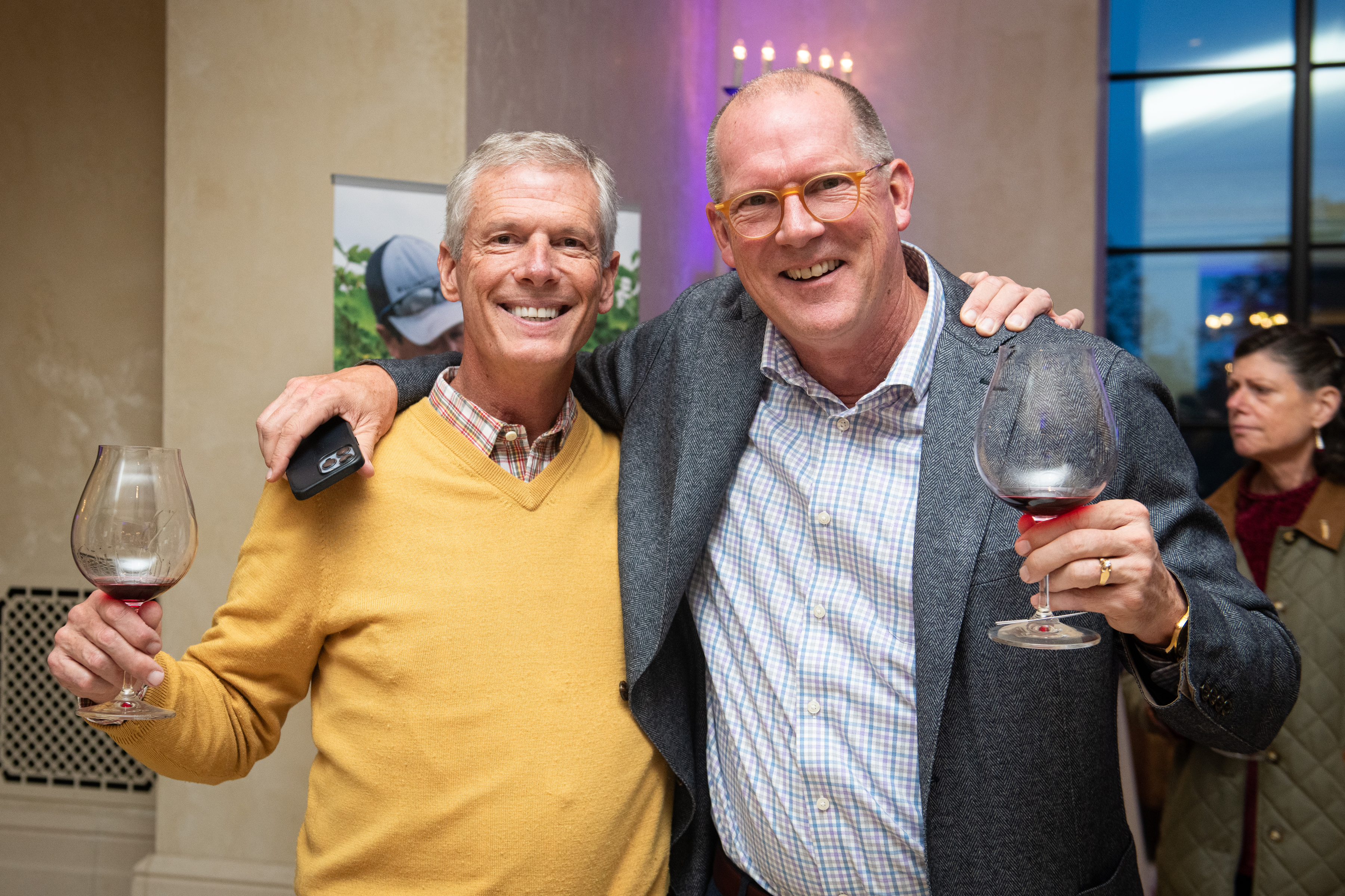 two men smiling and posing with glasses of wine